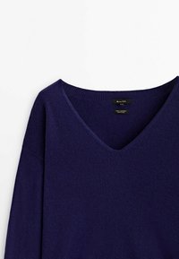 Pull en cachemire bleu marine avec un col en V, manches longues, texture douce et design minimaliste. Étiquettes visibles à l'intérieur du col.