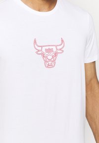 Camiseta blanca con un gráfico estilizado de cabeza de toro rojo centrado en el pecho, llevada por una persona de tono de piel clara.