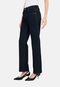 Jeans in denim blu scuro con una vestibilità a gamba dritta, cinque tasche, cuciture in vista e vita alta, abbinati a tacchi a spillo neri.