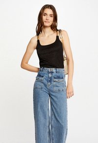 Black sleeveless top with a subtle shimmer, featuring gold chain accents on straps. Paired with high-waisted, light blue wide-leg jeans.