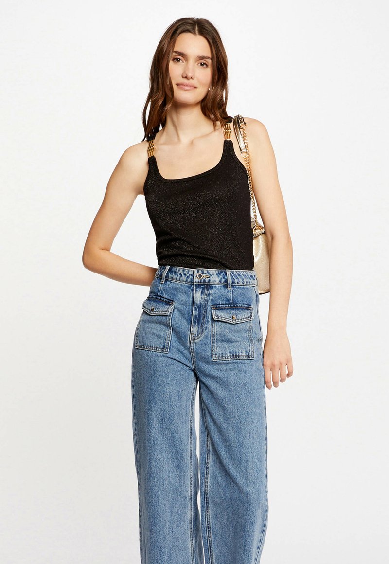Top senza maniche nero con una leggera lucentezza, caratterizzato da accenti di catena dorati sulle spalline. Abbinato a jeans a gamba larga azzurri a vita alta.