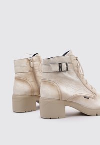 Botas de tobillo beiges hechas de cuero texturizado, con cremallera lateral, cierre de cordones y suela de goma ligera y gruesa; cuenta con detalles decorativos.