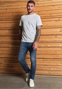 Graues Rundhals-T-Shirt kombiniert mit blauen Jeans und weißen Sneakers. Verfügt über kurze Ärmel, einen Standard-Schnitt und eine natürliche Stofftextur.