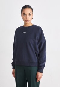 Felpa blu navy con vestibilità rilassata, polsini a costine e ricamo leggero sul petto. Tessuto in cotone morbido con una texture liscia.