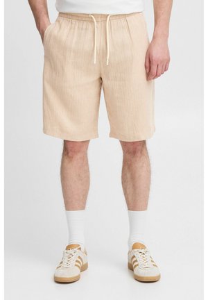 Shorts beiges avec un motif texturé et rayé, dotés d'une taille élastique et d'un cordon de serrage. Portés avec des chaussettes blanches et des baskets beiges.
