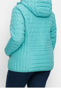 Světle modrá péřová bunda s prošívanou strukturou a kapucí. Má vertikální švy a boční kapsu na zip.