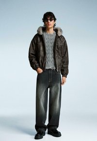 Brun fusk läder bomberjacka med foder av päls, grå kabelstickad tröja, mörka oversized jeans och svarta snörboots.