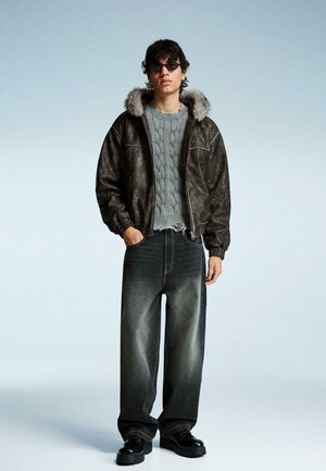 Hnědá umělá kožená bomber bunda s kapucí lemovanou kožešinou, šedý svetr s pleteninou do copánků, tmavé oversized džíny a černé šněrovací boty.