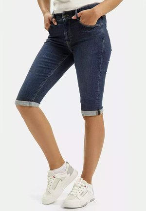 Dżinsowe szorty bermudy w ciemnoniebieskim kolorze z podwiniętymi mankietami, z dopasowanym krojem i pięcioma kieszeniami. W zestawie z białymi sportowymi trampkami.