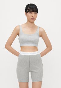 Šedá žeberní sportovní podprsenka a odpovídající bicyklové kraťasy, které mají bílý pás s logem Calvin Klein. Materiál je hladký a elastický.
