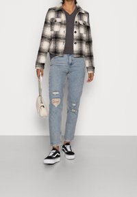 Gekürzte kariert Jacke in Schwarz und Weiß, kombiniert mit einem dunklen V-Ausschnitt-Oberteil und hellblauen, stark ausgewaschenen Jeans. Schwarze Sneakers und eine helle Handtasche.