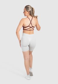 Sostenitore sportivo bordeaux con spalline e schiena scoperta, abbinato a pantaloni corti aderenti grigi chiari. La modella indossa scarpe da ginnastica bianche.