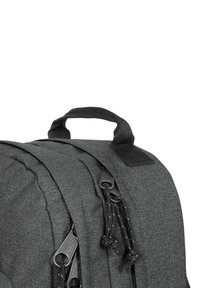 Mochila de tela gris con superficie texturizada, compartimentos con cremallera y un asa en la parte superior. Tiradores de cremallera negros con acentos de cordón.