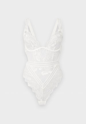 Λευκό κορμάκι από δαντέλα με λουλουδένια σχέδια, ρυθμιζόμενες τιράντες και βαθιά V λαιμόκοψη, σε απλό ανοιχτό φόντο.