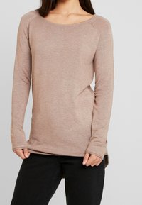 Ljust brunt långärmad tröja med rundad halsringning. Mjuk, strukturerad tyg, något längre baktill, åtsittande ärmar och sprund i sidorna.