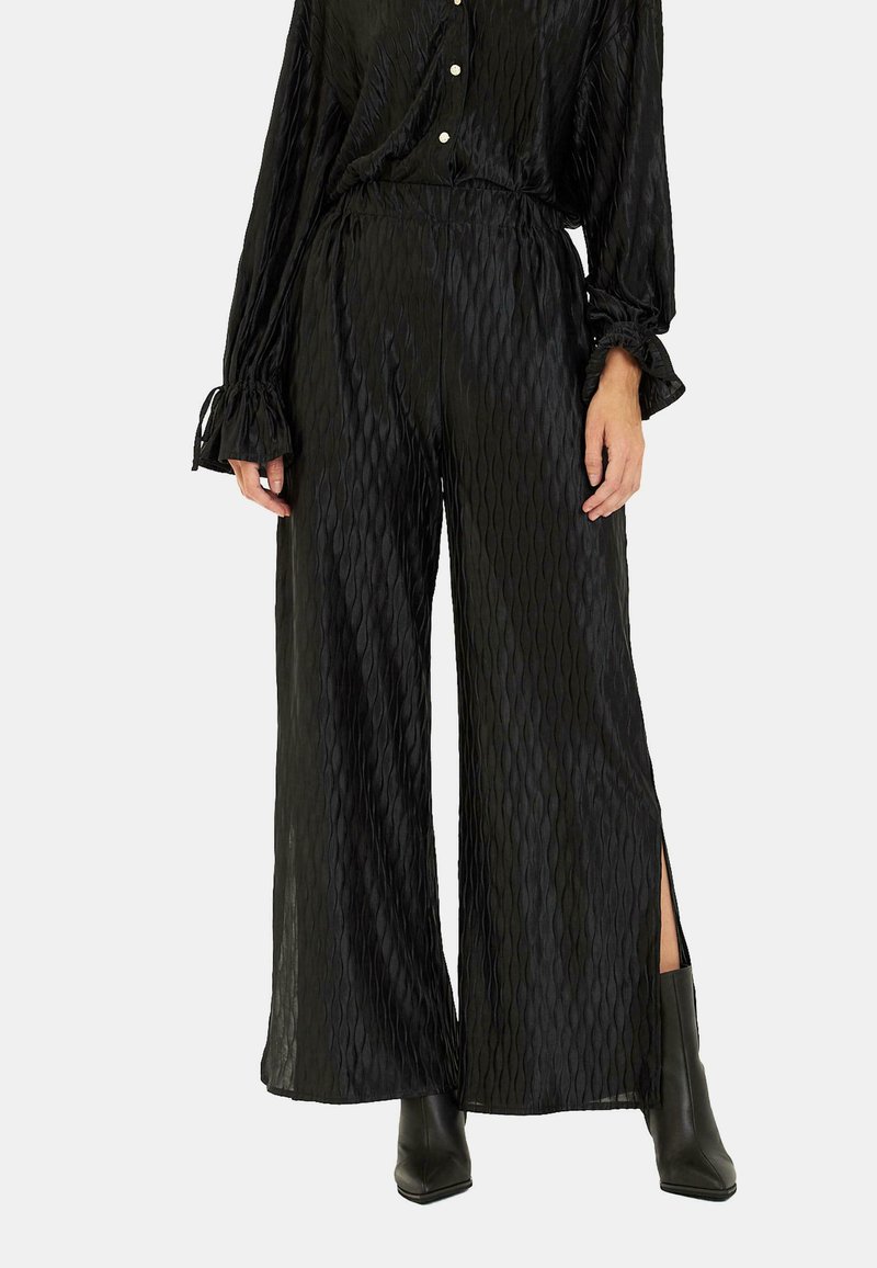 Czarne spodnie typu wide-leg z teksturowanym, diamentowym wzorem, z bocznymi rozcięciami. Wykonane z lekkiego materiału z elastycznym pasem.