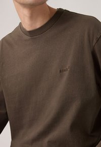 Tricou din bumbac maro, cu guler rotund. Textură moale, cu un mic logo brodat Levi's într-o nuanță mai închisă pe piept. Design simplu, croială relaxată.