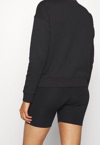 Sudadera negra hecha de una tela suave con puños acanalados, combinada con pantalones cortos negros ajustados. Ambas prendas tienen un diseño sencillo y una textura lisa.