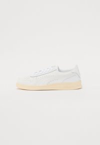 Baskets blanches en cuir avec des détails perforés, des lacets plats et une semelle en caoutchouc beige clair. Design minimaliste avec un branding discret.