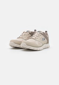 Zapatillas deportivas beige con parte superior de malla, cuello acolchado y suela de goma. Presentan detalles en gris y cordones para un ajuste seguro.