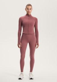 Mauve athletic set including a fitted zip-up long-sleeve top and high-waisted leggings with seamless construction and textured details.