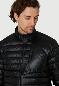 Sort pufferjakke med høj krave, horisontal quiltet design og lynlåslomme på venstre bryst, lavet af et skinnende, let materiale.