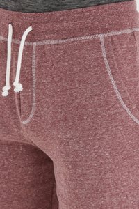 Pantalones de chándal color burdeos con una tela texturizada, que cuentan con cordones blancos, bolsillos laterales y detalles de costura en contraste.