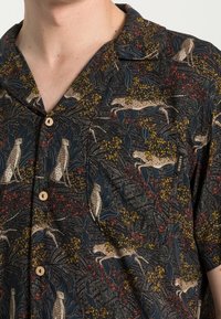Camicia a maniche corte con bottoni di colore nero, caratterizzata da una stampa naturale con leopardi, foglie e motivi floreali; realizzata in tessuto leggero.