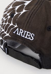 Melnā beisbola cepure ar baltu zirnekļtīkla rakstu sānos un "ARIES" izšuvumu baltā krāsā aizmugurē. Kokvilnas materiāls, regulējama siksna.