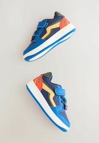 Jasnoniebieskie dziecięce sneakersy z kolorowymi akcentami, z rzepem i wesołym wzorem uśmiechu na pięcie, wyeksponowane na jasnym tle.