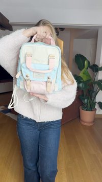 Pastel-colored backpack with a blue, cream, and pink design. Features adjustable straps, two front pockets, and metal hardware accents.