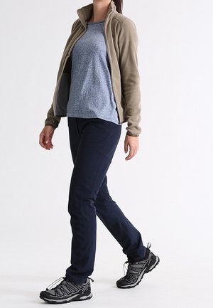 Veste en polaire beige, haut à manches courtes bleu, pantalon marine et chaussures de randonnée noires. Comprend un zip sur le devant et des matériaux texturés.