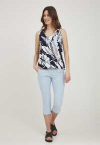 Halenka bez rukávov s kvetinovým vzorom v námorníckej, bielej a svetlomodrej farbe, spárovaná so svetlomodrými skrátenými nohavicami a čiernymi sandálmi.