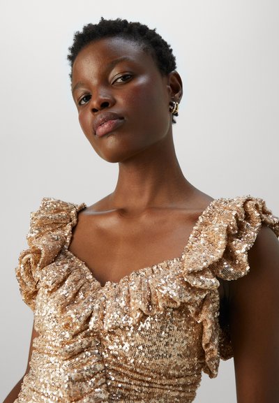 Robe en sequins dorés avec des détails de épaules froncées, présentant un corsage ajusté et une texture douce, créant une apparence scintillante et superposée.