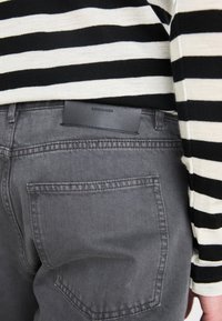 Chemise à manches longues à rayures noires et blanches associée à un pantalon en denim gris foncé. Présente une étiquette en cuir noir avec l'inscription "COPENHAGUE."