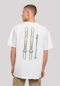 White t-shirt featuring a graphic of three silver metal clips on the back. Short sleeves and relaxed fit with a round neckline.