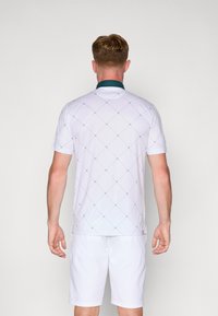 Hvid kortærmet skjorte med diamantskærm og turkis krave, parret med hvide shorts. Stoffet virker let og glat.