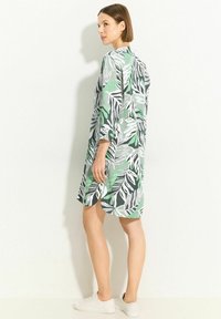 Long, loose-fitting dress in green, white, and black with leaf patterns. Features three-quarter sleeves and side slits. Textured fabric.