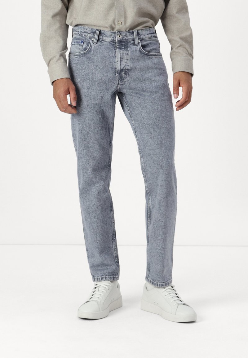 Jeans rectos de color azul claro con textura desgastada, diseño de cinco bolsillos, costuras visibles y cierre de botón, combinados con zapatillas blancas.