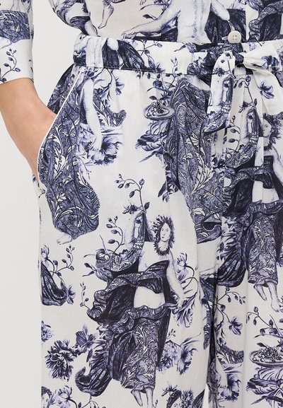 Bijele hlače od tkanine sa plavim botaničkim i figurativnim uzorcima, s pojasom na vezanje, bočnim džepovima i mekanim, teksturiranim materijalom.