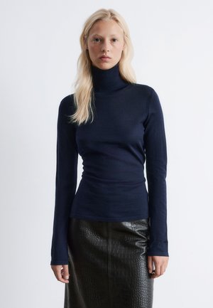 Navy turtleneck sweater made of a soft, stretchy fabric, featuring long sleeves and a fitted silhouette. Worn with a black textured leather skirt.