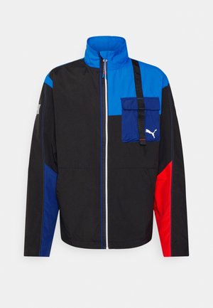 Schwarze, blaue und rote Jacke mit Reißverschluss, hohem Kragen, Fronttasche auf der Brust mit Klappe und Puma-Logo in der unteren rechten Ecke der Tasche.