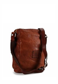 Bruine leren crossbodytas met een gestructureerde afwerking, een ritssluiting aan de bovenkant en een bruine schouderriem; heeft een rechthoekig label aan de voorkant.