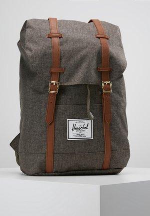 Bruine stoffen rugzak met twee leren bandjes en gespen, voorzien van een voorvak en een wit rechthoekig Herschel merklabel.