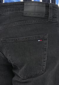 Mustad mustritooted teksad on varustatud väikese triibulise logoga tagakotil ja ristküliku kujulise musta nahkplaadiga vöökohtades.