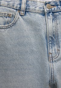 Jean en denim bleu clair avec coutures visibles, passant de ceinture, poche avant, petite poche à monnaie et fermeture par bouton métallique à la taille.