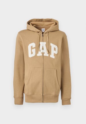 Tan zip-up hoodie featuring a front pocket and white "GAP" logo. Made from soft fabric with ribbed cuffs and hem.