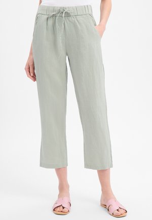 Pantalon court en lin vert sauge clair avec taille élastique et cordon, poches latérales, porté avec des sandales slides roses et un haut blanc.