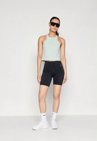 Top curto verde claro com ligeiro brilho, calções de ciclismo pretos de cintura alta com detalhes de costura e sapatilhas brancas de desporto.