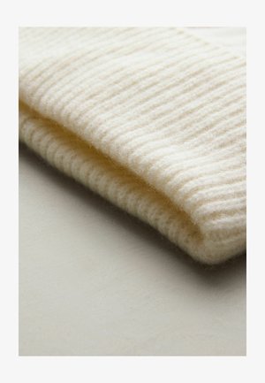 Vit stickad mössa i mjuk, strukturerad ull, med ett ribbat mönster och en vikt uppkant i botten.